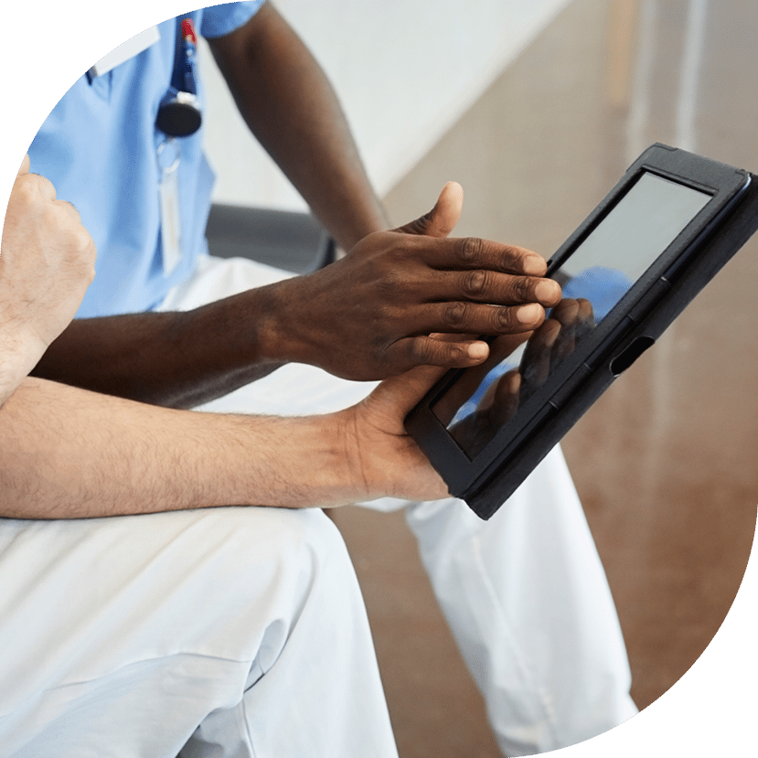 Zwei Personen aus dem Gesundheitssektor schauen in ein Tablet. Eine Person hält das Tablet mit einer Hand, während eine andere Person das Tablet bedient.